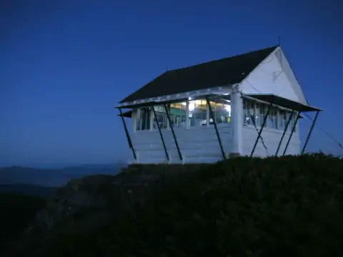 A fire lookout tower stands on a ridge at dusk.
