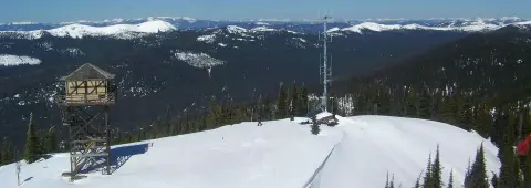 A snow-covered mountain peak with a lookout tower and a communication tower.