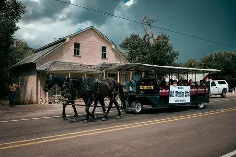 A horse-drawn carriage carries passengers past a historic pink building.