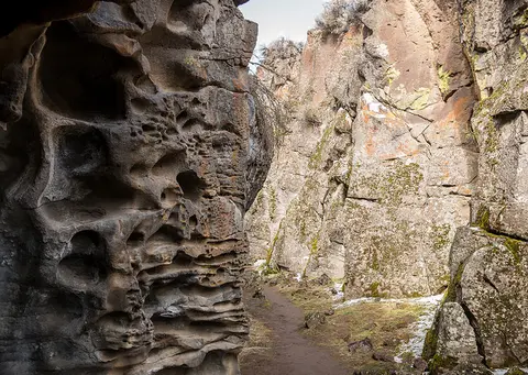 A narrow dirt path winds between rocky walls with weathered formations.