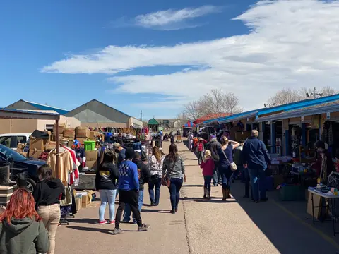 People walking along an outdoor market between rows of booths on a sunny day.