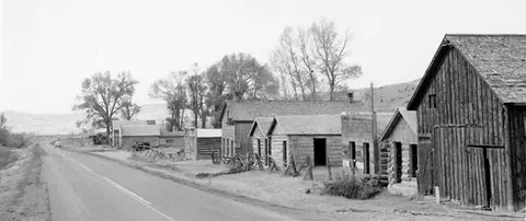 Black and white historic photograph of a row of old wooden buildings alongside a road.