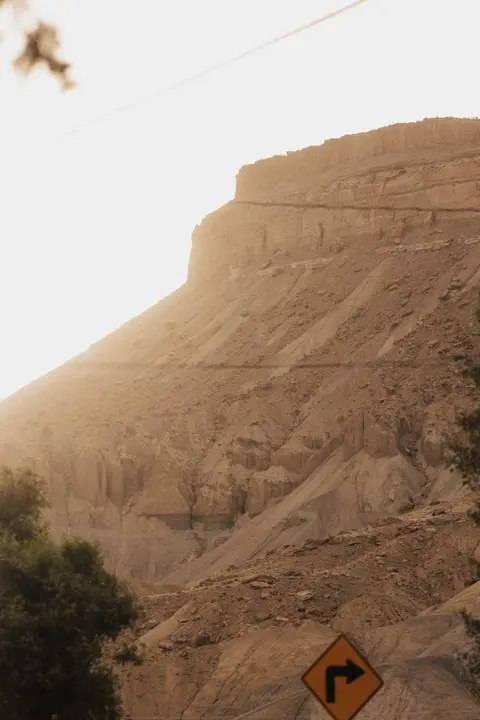 A rugged cliffside illuminated by warm sunlight with a road sign at the bottom right.