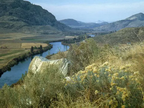 A winding river flowing through a valley surrounded by hills and mountains.