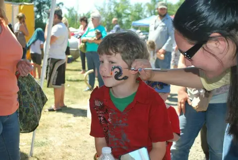 A child gets his face painted at an outdoor gathering.