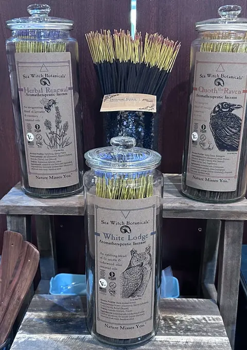 Glass jars and a container filled with various types of incense sticks on a wooden shelf.