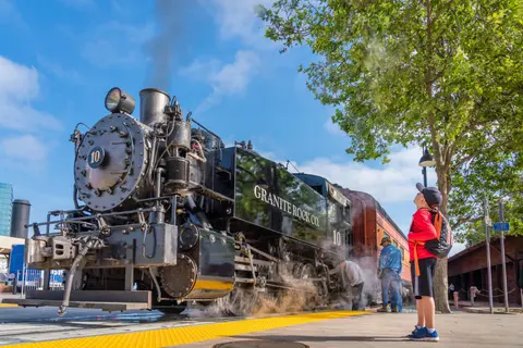 A child looks up at a large steam locomotive on display near a platform.