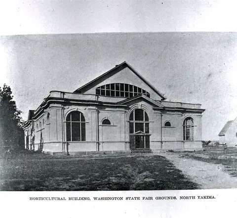 Black and white historic photograph showing the exterior of a building with arched windows and a large gable roof.
