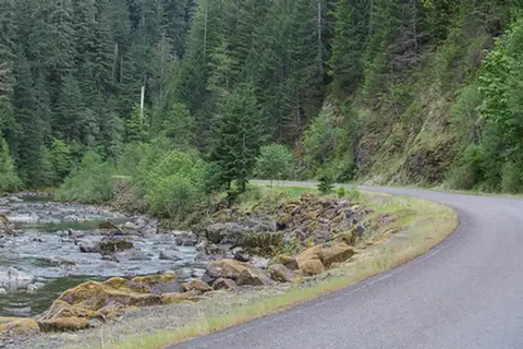 A winding road runs alongside a rocky river through a forest.