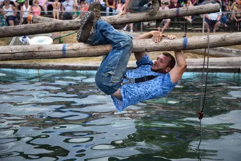 A man hangs from a log above a pool of water during a lumberjack competition.