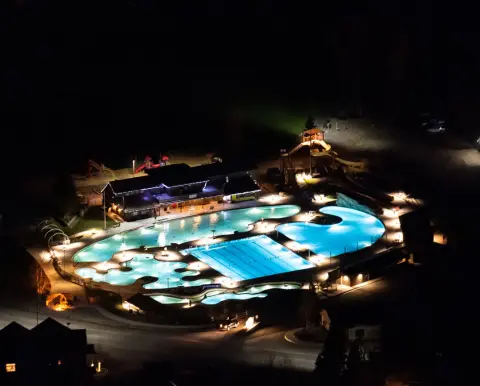 An elevated night view of a brightly lit outdoor swimming pool complex.
