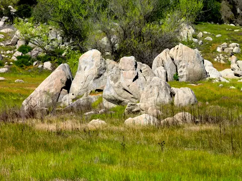 A field of green grass with large rock formations and trees.