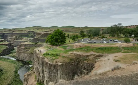 A scenic view of a deep canyon with a river flowing at the bottom under a cloudy sky.
