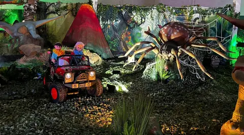 A toy jeep carrying dolls is parked in a jungle-themed display with a large spider and a volcano backdrop.