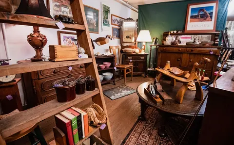 An interior view of a cluttered antique shop with wooden furniture, shelves, and various decorative items.