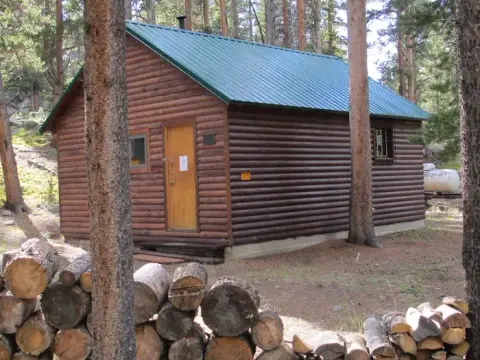 A log cabin with a green metal roof stands in a wooded area.