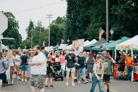 A large crowd of people gathers at an outdoor street fair with food tents and booths.