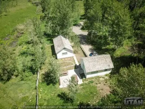 An aerial view shows two small cabins nestled in a wooded, grassy landscape.