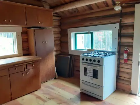 An interior view of a rustic cabin kitchen with wooden walls and a white stove.