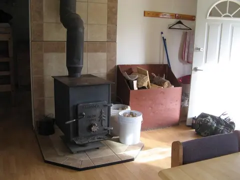 A wood stove is in the corner of a room with a box of firewood.