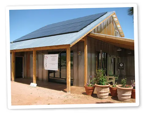 Exterior view of a metal building with solar panels on the roof and potted plants in front.