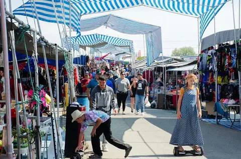 A busy outdoor market filled with shoppers walking under striped canopies.