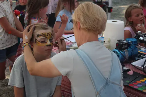 A face painter applies tiger makeup to a child's face.