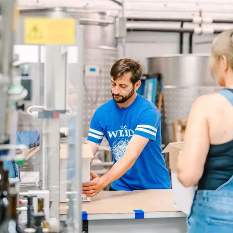 A man in a blue shirt packs boxes in an industrial interior.