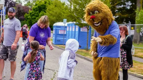 A costumed mascot interacts with children outdoors at an event.