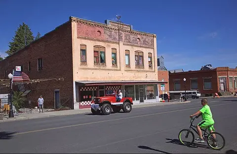 A street scene with a historic building, a red vehicle, and a person riding a bicycle.