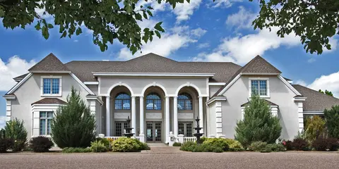 Exterior view of a large modern house with columns and a landscaped front yard.