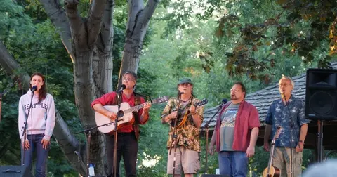 A band performs outdoors with instruments and microphones.