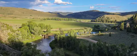 A wide landscape view of a river, bridge, and green valley under a partly cloudy sky.