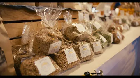 Bags of grains and lentils are displayed on a shelf in a market.