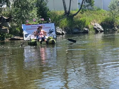 A person rows a small inflatable watercraft on a river.