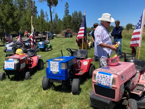A row of decorated lawn mowers with American flags parked in a grassy field.