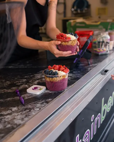 A person handing over a fruit and acai bowl across a counter.