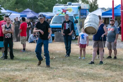 People participate in an outdoor event with tents, a food truck, and a flying keg.