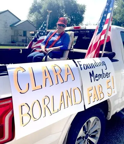 A woman sits in the bed of a pickup truck decorated with flags and signs.