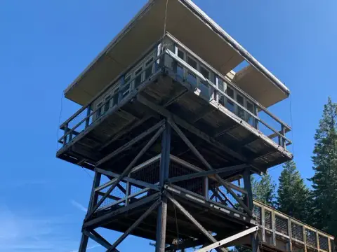 A tall wooden fire lookout tower stands against a clear blue sky.