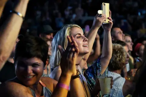 A woman in a crowd raises her phone to record at an event.