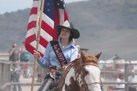 A cowgirl on horseback carries an American flag.