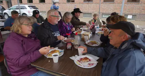 A group of people are eating a meal together at long outdoor tables.