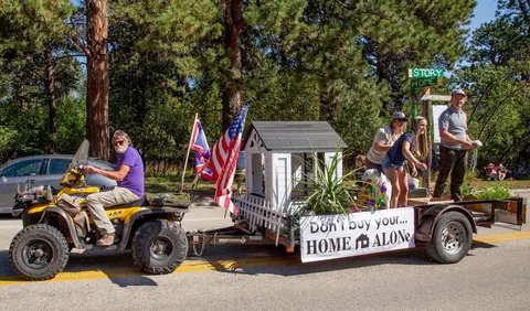 A parade float pulled by an ATV on a street lined with trees.