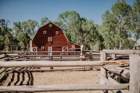 A red barn stands behind a wooden fence with a horse nearby.