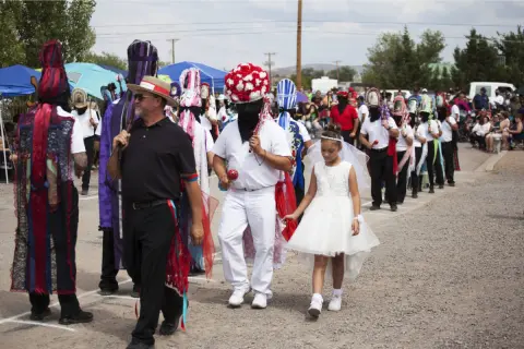 People in costumes and festive attire participate in a cultural parade outdoors.