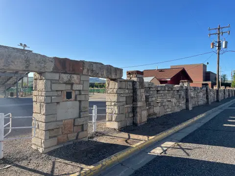 A long stone wall and gateway run along a street with a yellow curb.