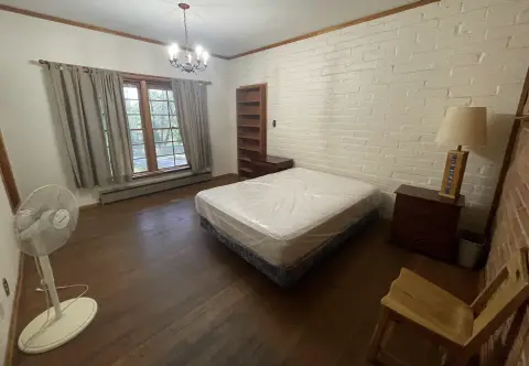 A bedroom interior with a mattress, wooden floors, a white brick wall, and a window with curtains.