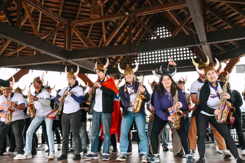 A group of musicians wearing Viking helmets play saxophones under a wooden pavilion.