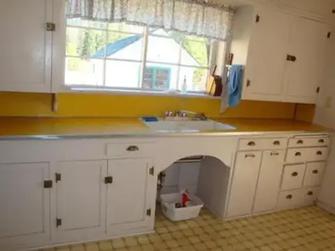 A kitchen with white cabinets, yellow walls, and a sink under a window.